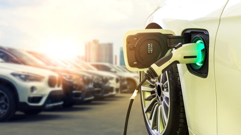 A yellow electric vehicle charging in a car park, a row of BMW cars to one side.